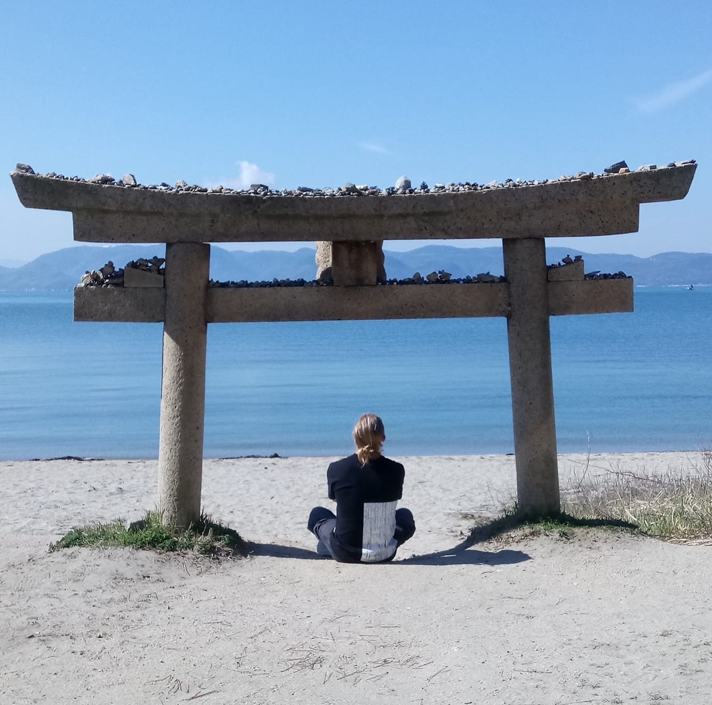 A relaxing beachside scene beneath a stone Shinto torii gate covered with stones left by believers on the art island of Naoshima